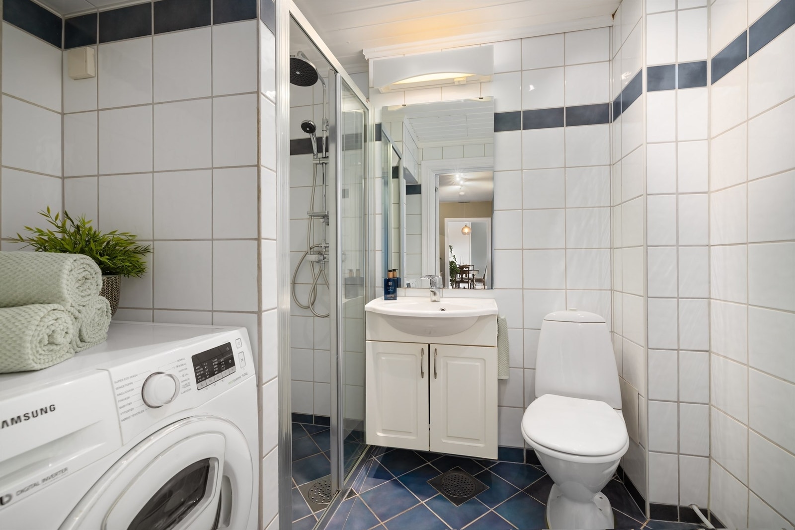 Videre er det praktisk dusjnisje separert med skyvedør av glass tilkoblet både hånddusj og rainshower, gulvstående toalett og opplegg for vaskemaskin Galleribilde