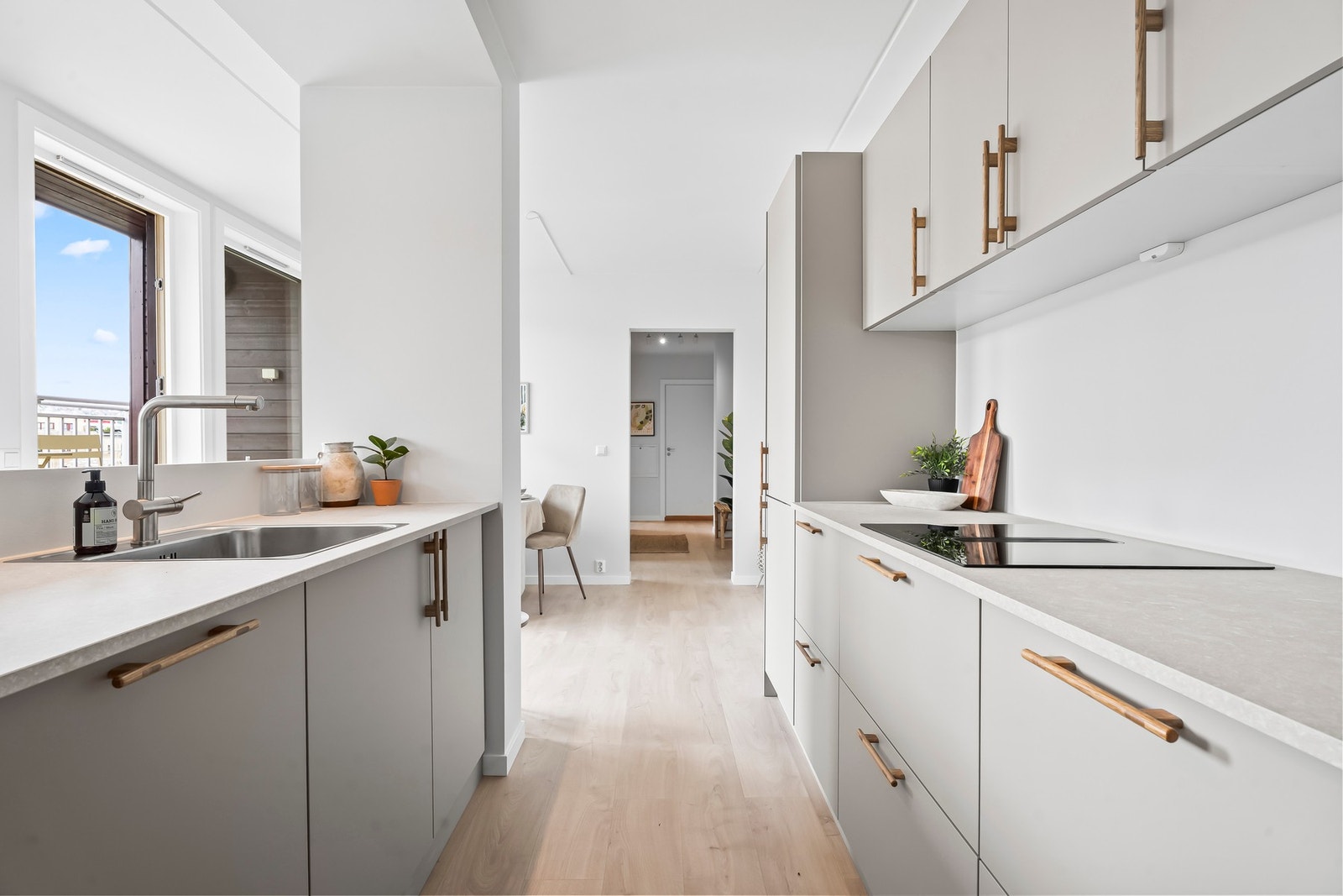 Grå fronter og benkeplate i lys laminat, kombinert med åpne hyller i eik. Kjøkkenet er plassert parallelt langs innerste veggen og delt av mot tv-stuen uten å miste lys og romfølelse. Galleribilde