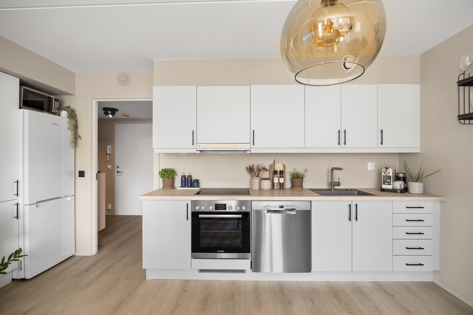 Lyst og tidløst kjøkken med enkle, slette fronter og integrerte hvitevarer for et rent uttrykk. Her er det kun kjøleskapet som står fritt. Galleribilde