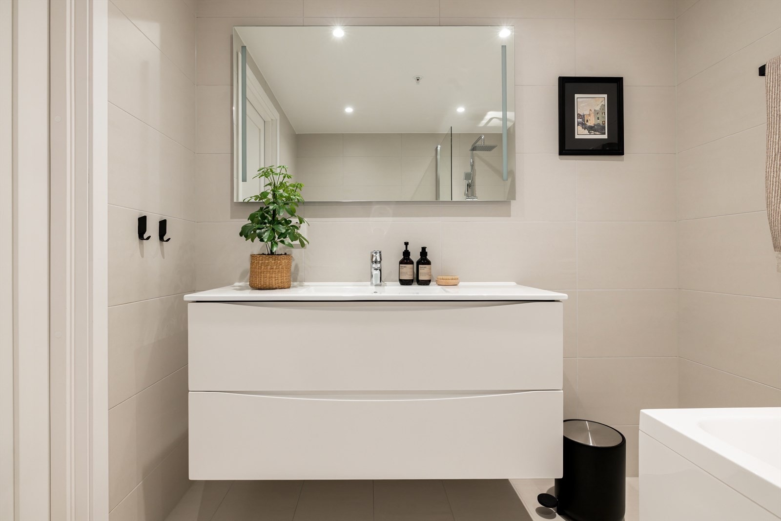 Innredningen består av en heldekkende servant på hvit skuffeseksjon, speil med integrert belysning og et veggmontert toalett. Rommet er påkostet med et badekar som har både regnfallsdusj, hånddusj og dusjvegg. Galleribilde