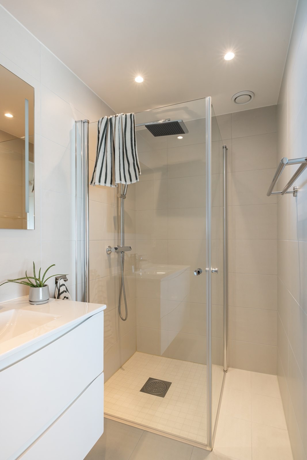 Hovedbadet er innredet med lysbeige fliser på både gulv og vegger, og har behagelig gulvvarme samt downlights i himlingen. Rommet er utstyrt med dusjhjørne med innfellbare glassdører, regnfallsdusj og separat hånddusj. Galleribilde