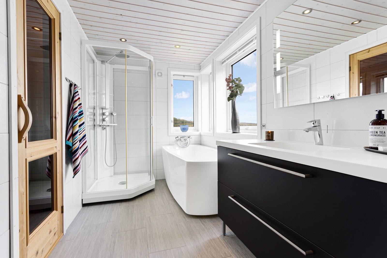 Begge badene er utført med moderne, grå fliser på gulv og lyse fliser på vegg. Det største baderommet har servant i innredning, vegghengt toalett, badekar og dusjkabinett. Galleribilde
