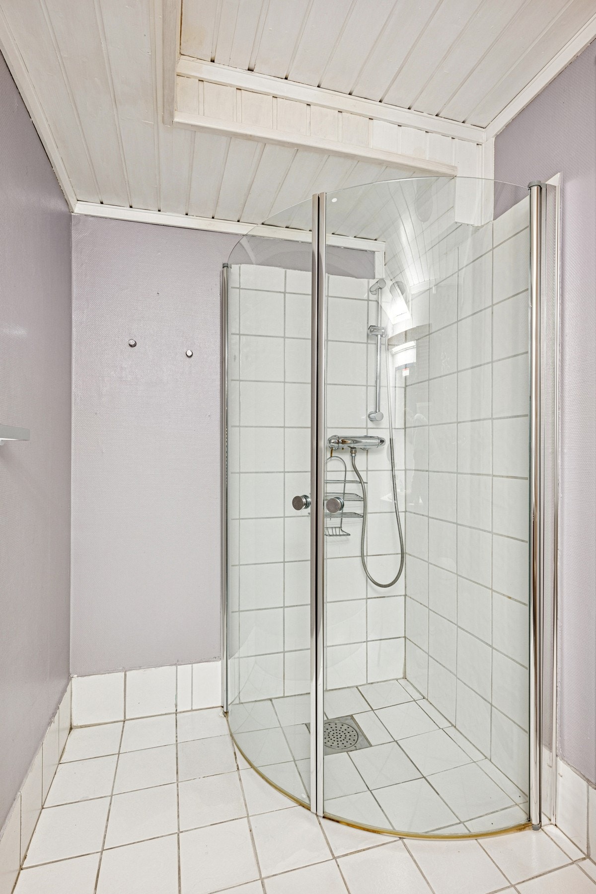 Badet er utstyrt med dusjhjørne med svingbare glassdører og flislagte vegger Galleribilde