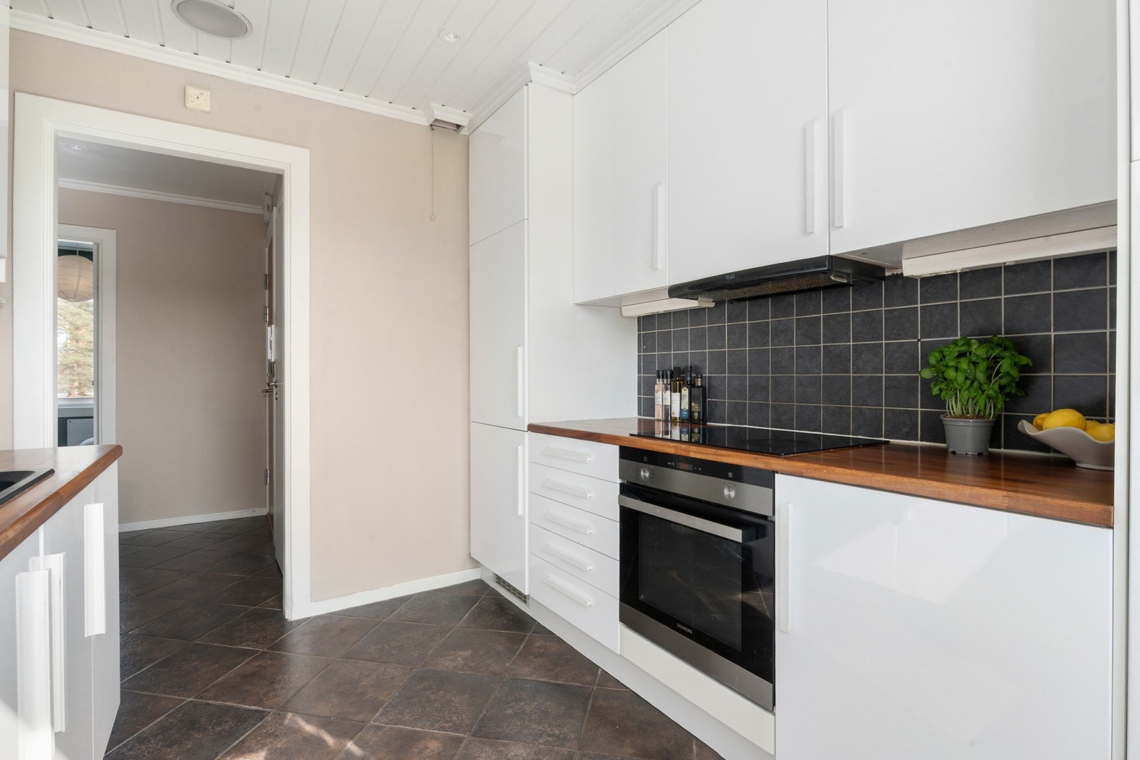 Takhøy kjøkkeninnredning fra IKEA med glatte høyglans skapfronter og nyere håndtak fra 2020, vitrineskap, heltre benkeplate med fliser på bakvegg, oppvaskkum med benkebeslag, og ventilator. Galleribilde