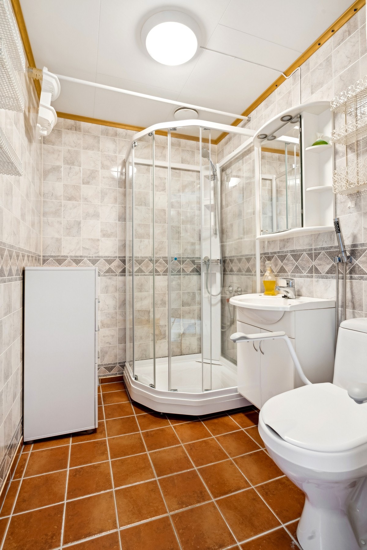 Baderommet har vegger med baderomsplater, himling med lyse himlingsplater og gulv belagt med stilrene fliser Galleribilde