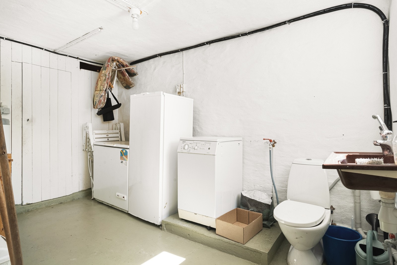 Rommet har malt betonggulv og inneholder vask, varmtvannstank, opplegg for vaskemaskin og ekstra toalett. Galleribilde