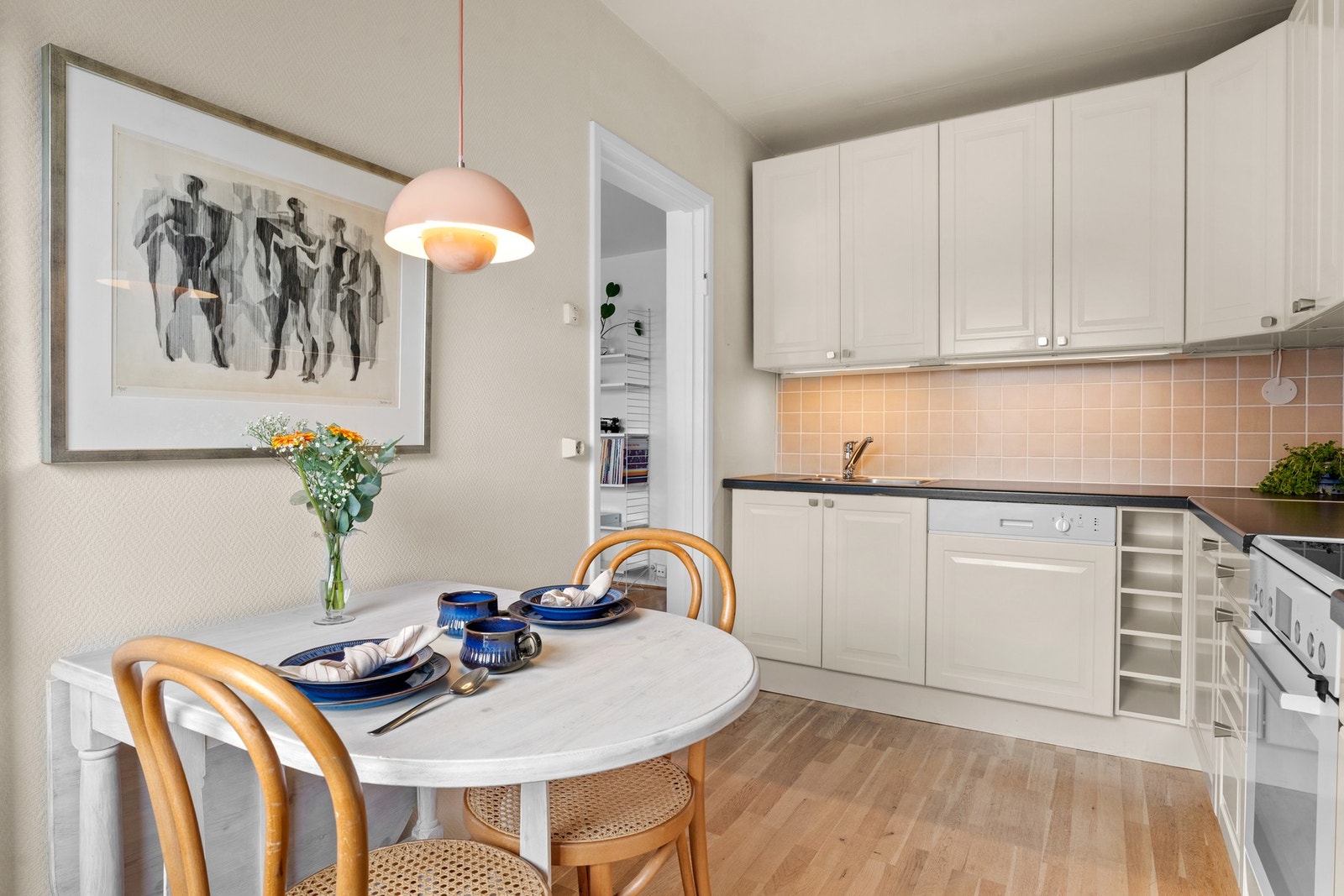 Rommet har eikeparkett på gulvet, lysmalte vegger og det er montert fliser på veggene mellom benk og overskap. Lys under overskapene for arbeidsbelysning. Galleribilde