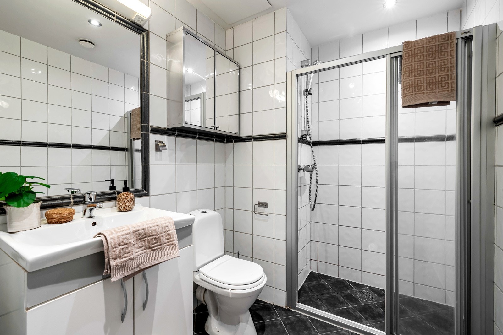 Badet er innredet med dusjhjørne med glassdør, toalett, servant med underskap, speil med belysning og et ekstra overskap med speil over toalettet. Galleribilde