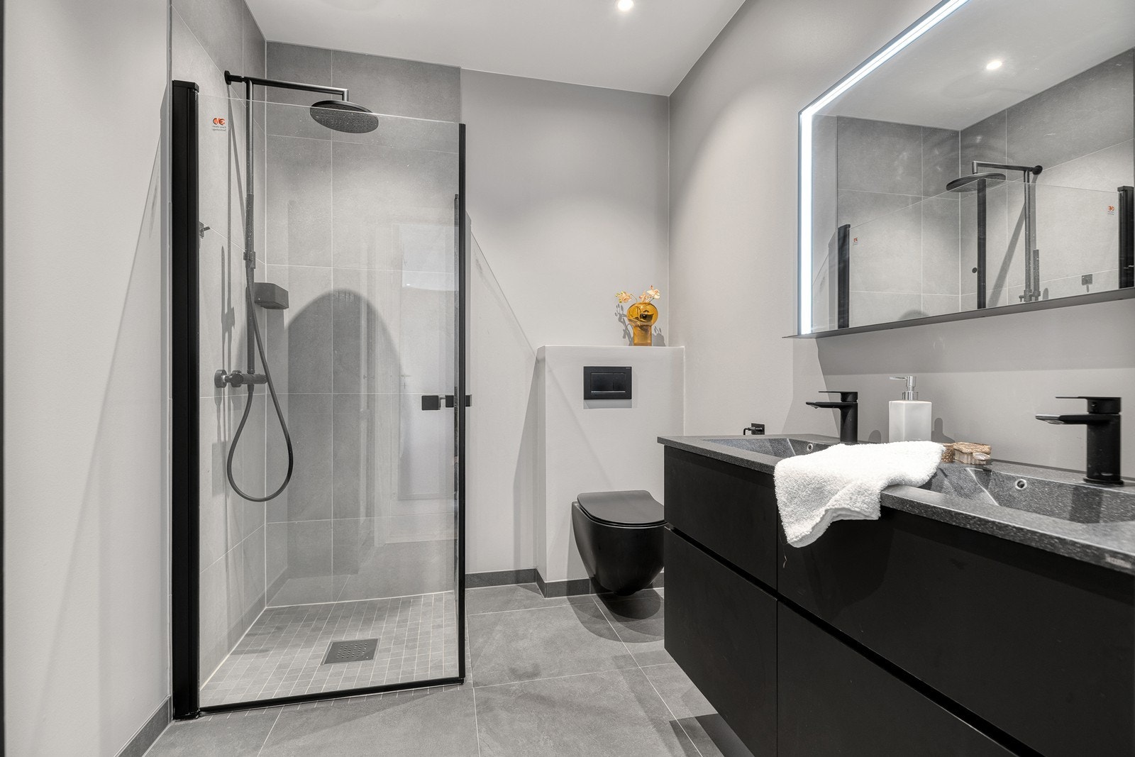 Lyst og flott bad med flis på gulv m/oppkant - innredet med dobbel servant, dusjhjørne og veggmontert toalett Galleribilde