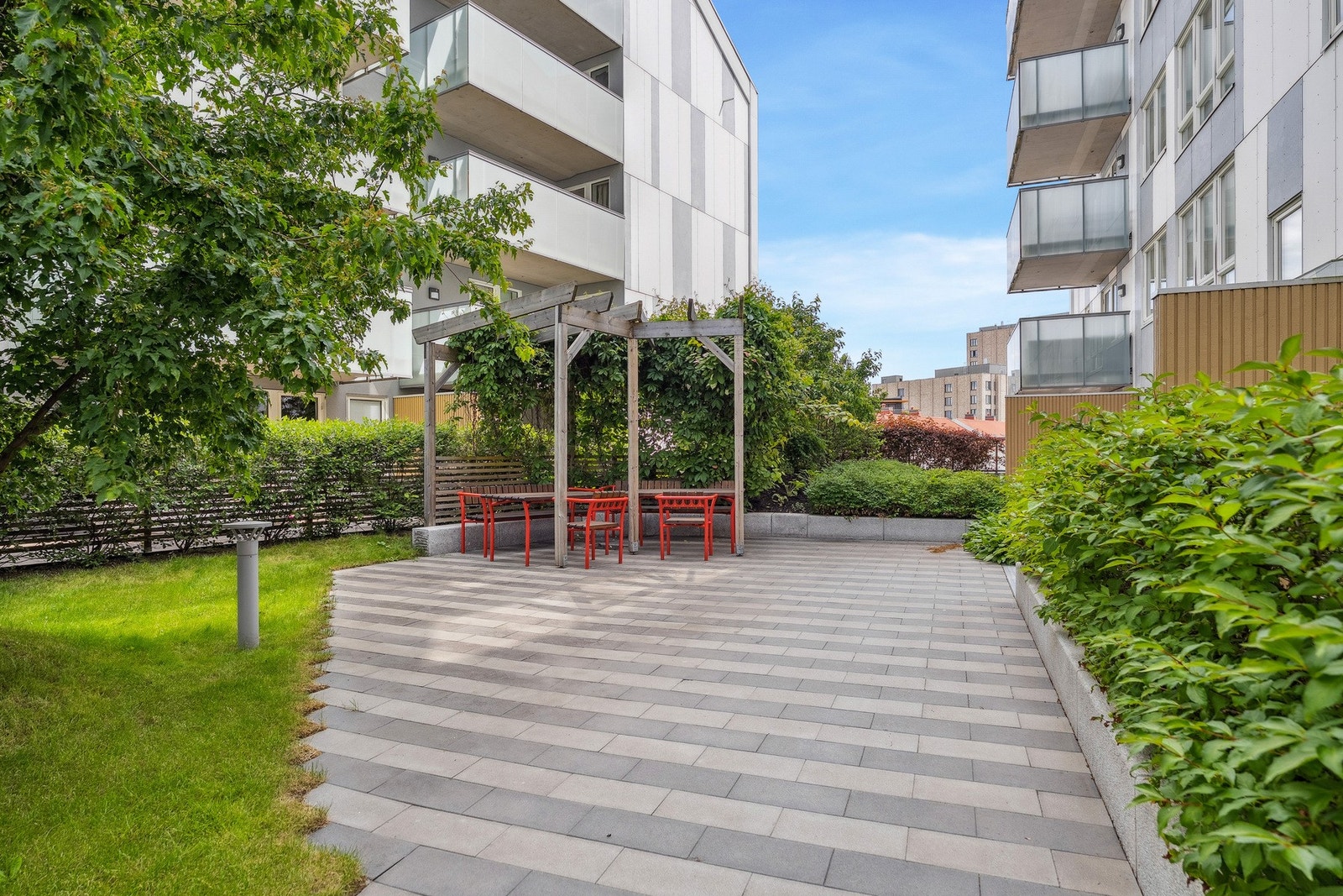 Velstelt og skjermet fellesområde med sittegrupper og grønt beplantet ramme. Galleribilde