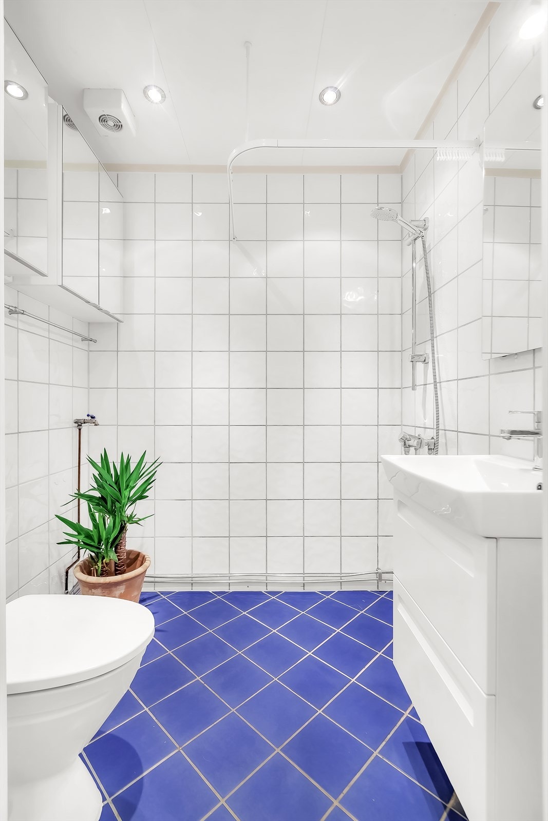 Leiligheten har et flislagt bad med frittstående toalett, dushjørne, speilskap på to vegger og servant med underskap. Galleribilde