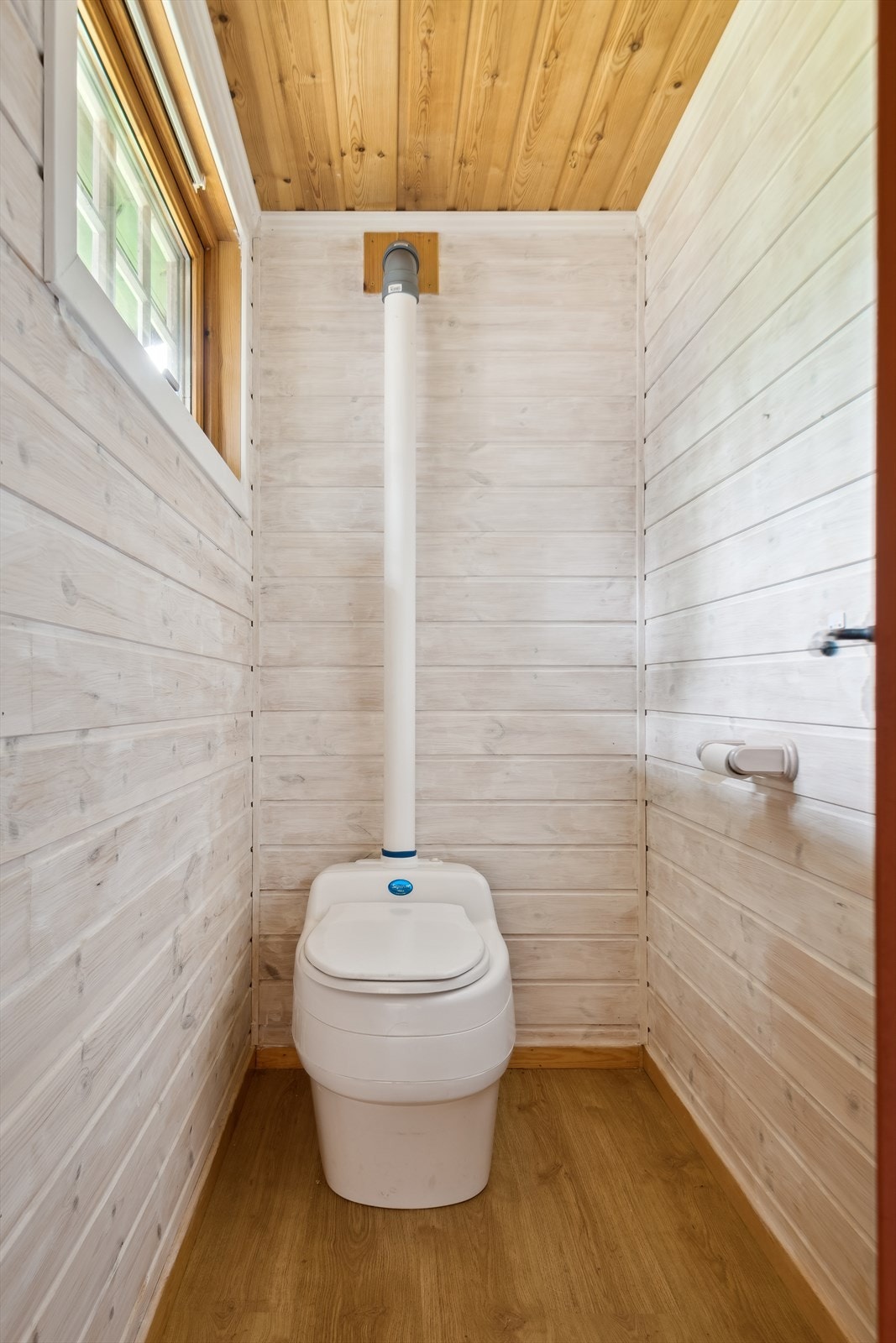 Separat toalettrom med laminat på gulvet og beiset panel på veggene. Rommet er utstyrt med et Separett biodo, som har lufterør ført ut gjennom veggen og over tak. Rommet mangler tilluftsventilering, som er grunnlaget for TG2. Galleribilde