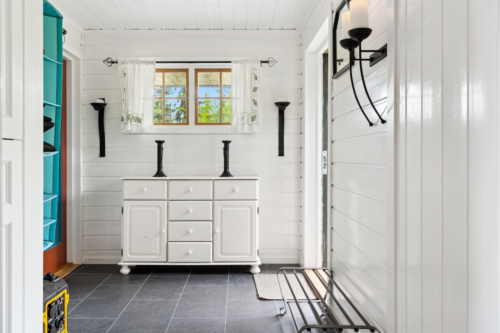 Inngangspartiet er tilknyttet en veranda på terrengnivå via en liten tretrapp. Lysmalt entré med god plass til å henge fra seg yttertøyet. Fra entreen er det adkomst inn til stuen. Galleribilde