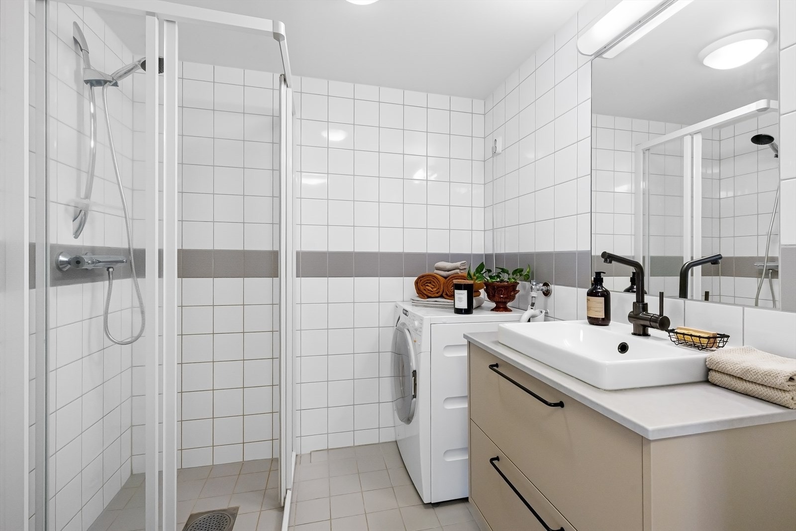 Romslig bad med dusjhjørne, wc, servant med skuffer, speil og opplegg for vaskemaskin. Galleribilde
