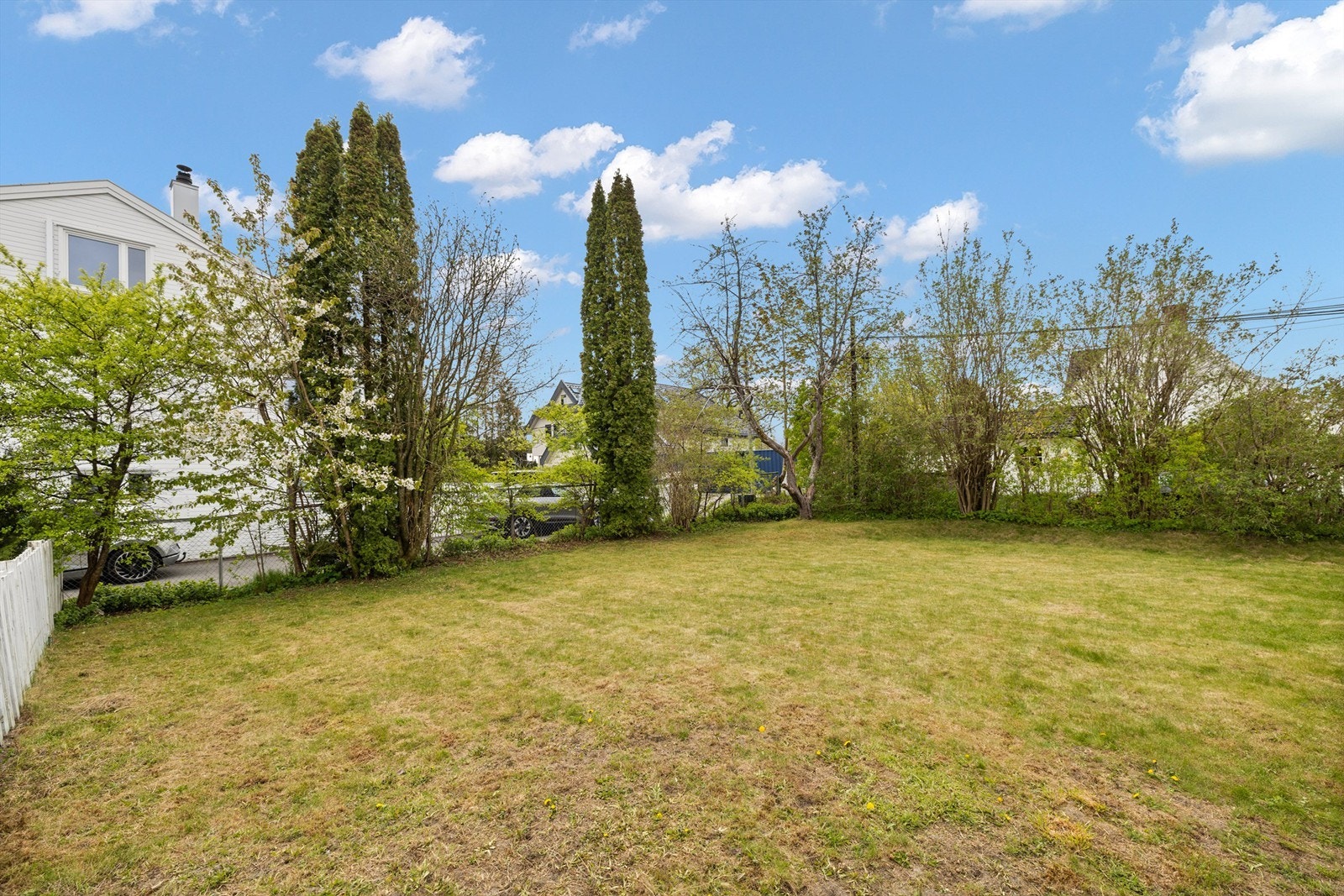 En romslig og forholdsvis flat tomtedel som er opparbeidet med gressplen og beplantning Galleribilde