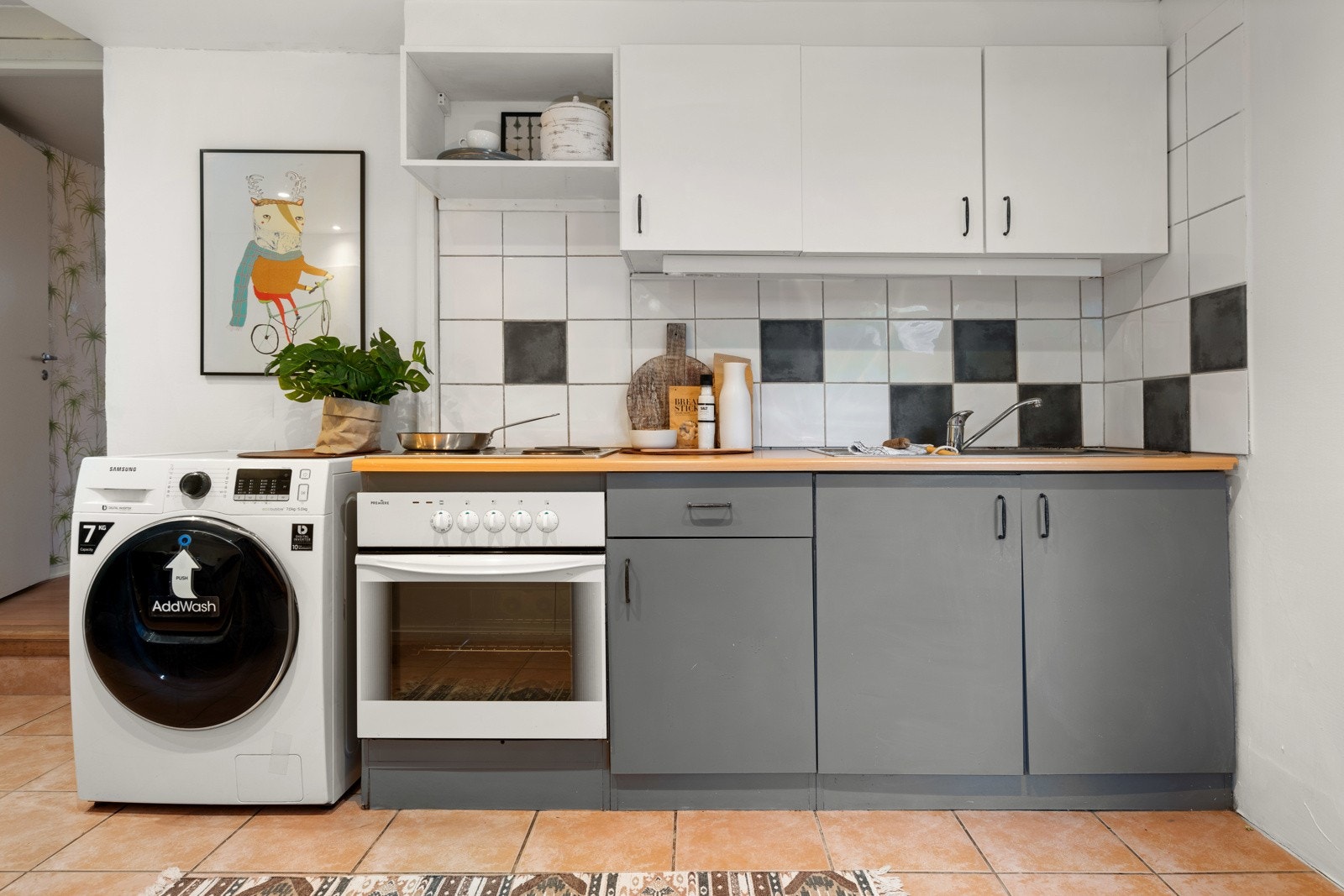 Det er slette fronter, fliser over benkeplate av laminat, nedfelt oppvaskkum av rustfritt stål, i tillegg til belysning og stikkontakt under overskap. Galleribilde