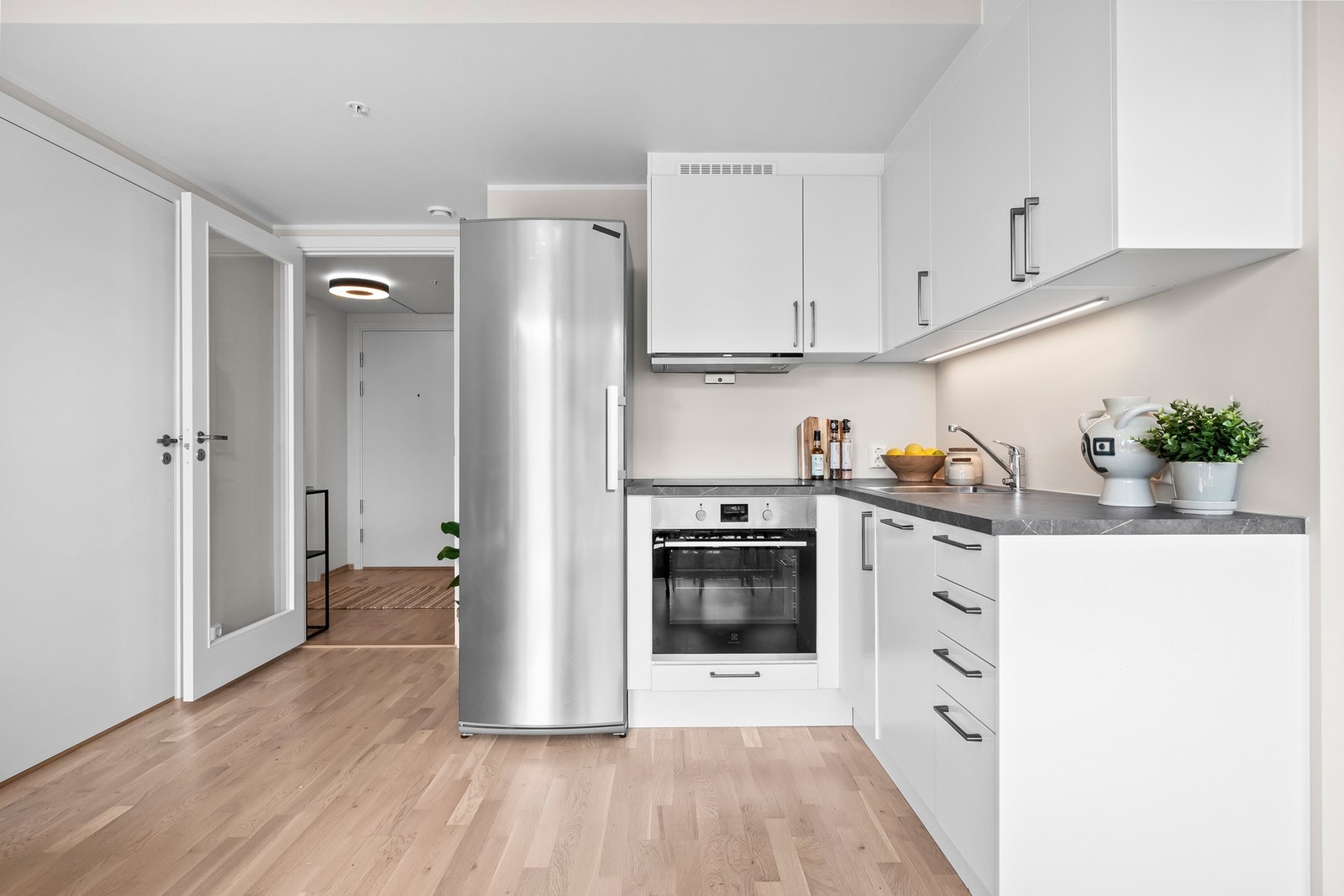 Integrerte hvitevarer som induksjonsplatetopp, stekeovn, oppvaskmaskin og frittstående kjøle-/fryseskap. Galleribilde