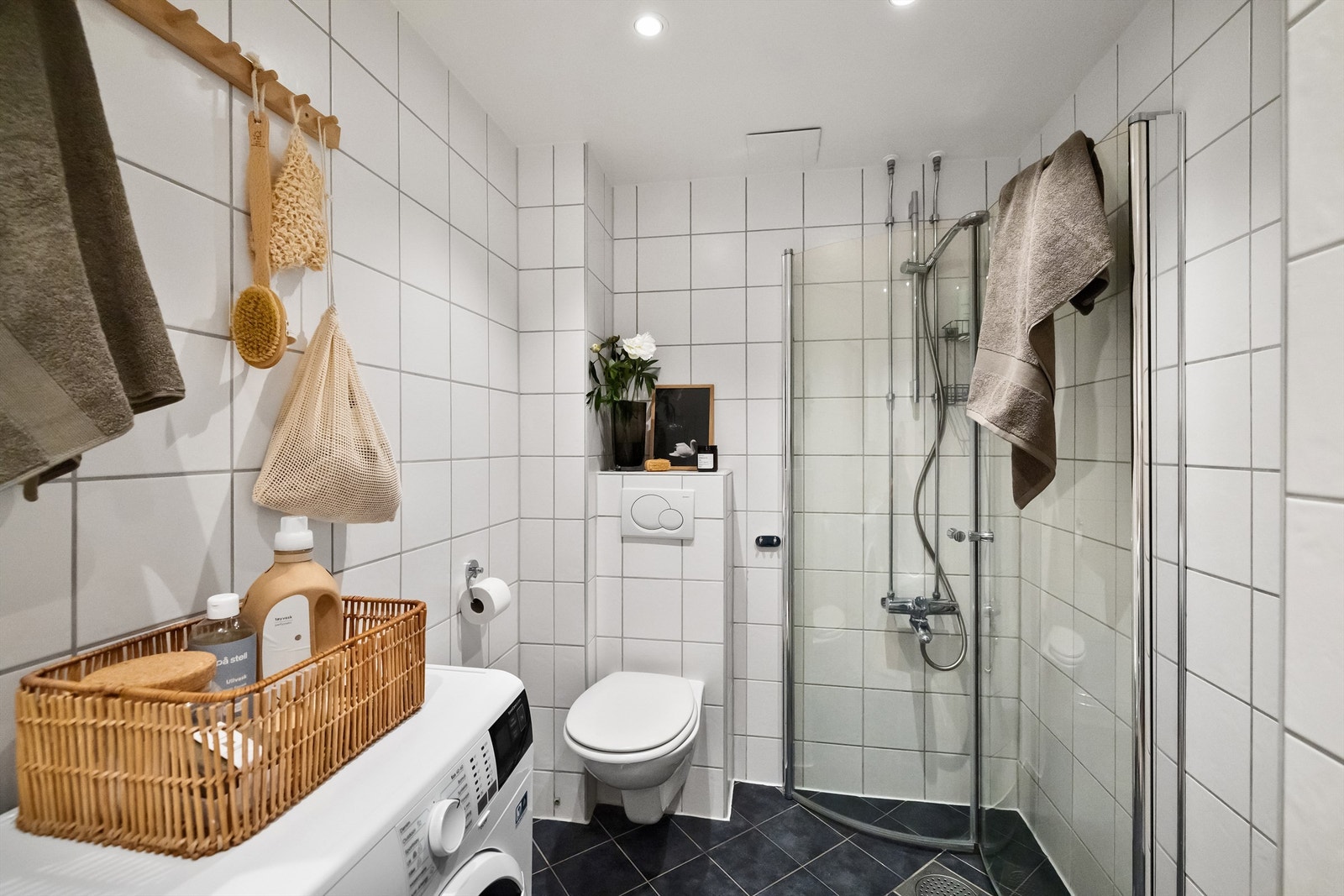 Badet er utstyrt med vegghengt toalett, dusjhjørne med innfellbare glassdører, heldekkende servant med skapinnredning under og speilskap på vegg Galleribilde