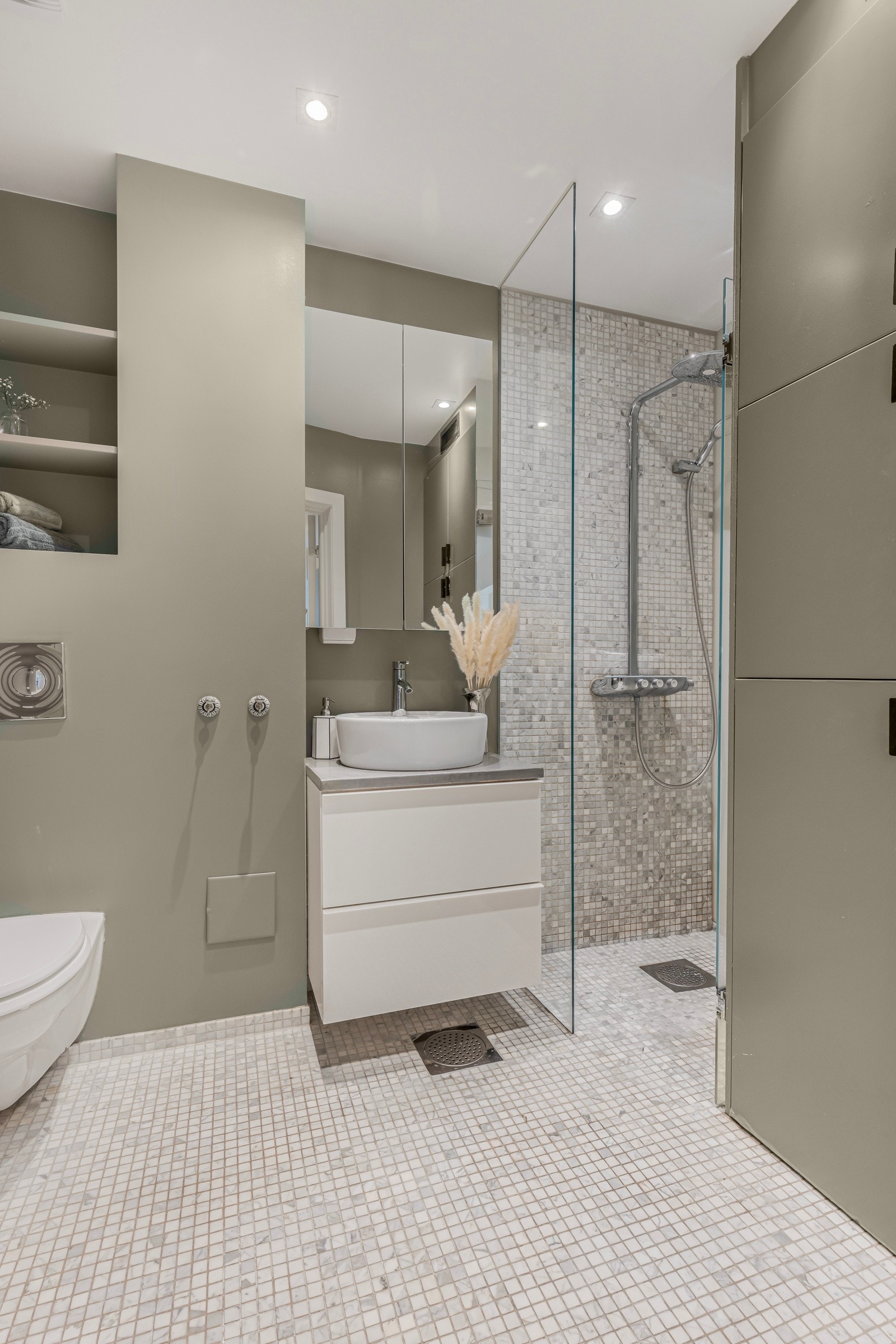 Meget delikat baderom bestående av vegghengt toalett, servant, dusjhjørne og integrerte hyller til oppbevaring/pynt. Galleribilde