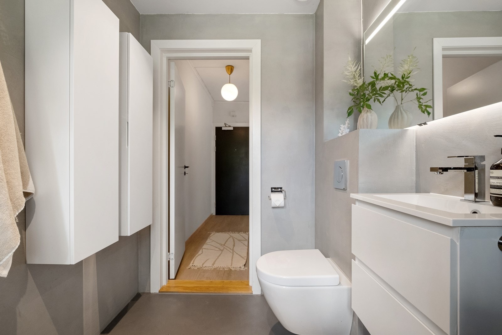 Badet er utstyrt med vegghengt toalett, servant integrert i baderomsinnredning, speil med belysning og dusjhjørne med svingbare glassdører Galleribilde