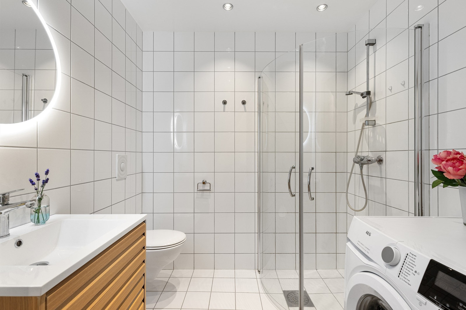 Tidløst og flislagt baderom fra byggeår med gulvvarme, opplegg til vaskemaskin, dusjhjørne, vegghengt toalett og servant. Badet ble oppgradert med nytt servantmøbel og speil i 2025 Galleribilde