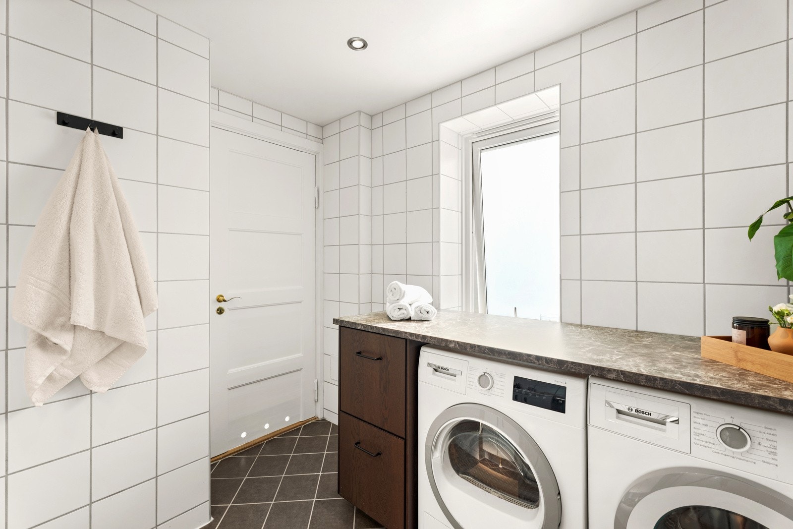 Badet er utstyrt med dusjhjørne med innfellbare glassvegger og servantinnredning med under- og overskap. Det er også opplegg og plass til vaskemaskin og tørketrommel. Galleribilde