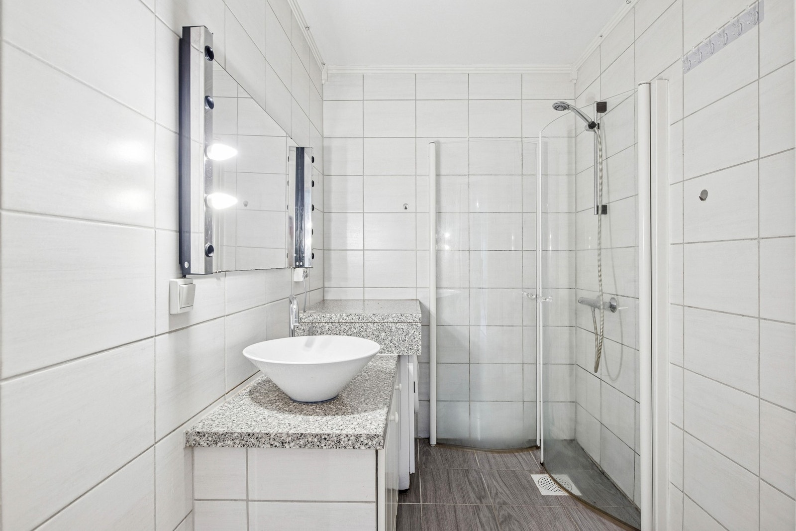 Badet er helfliset og innredet med dusjhjørne med buede dører, servant med speil og belysning, samt frittstående toalett. Galleribilde