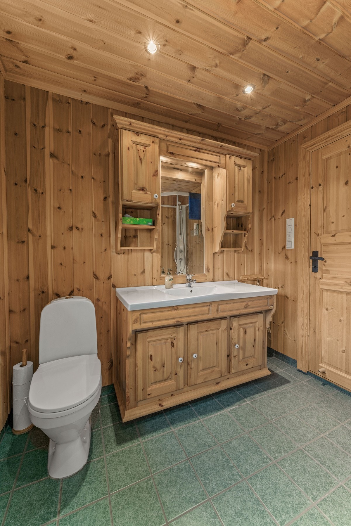 Det nyeste badet har panel på vegger og tak, dusjkabinett, servant med speil og overskap - samt elektrisk avtrekksvifte. Galleribilde