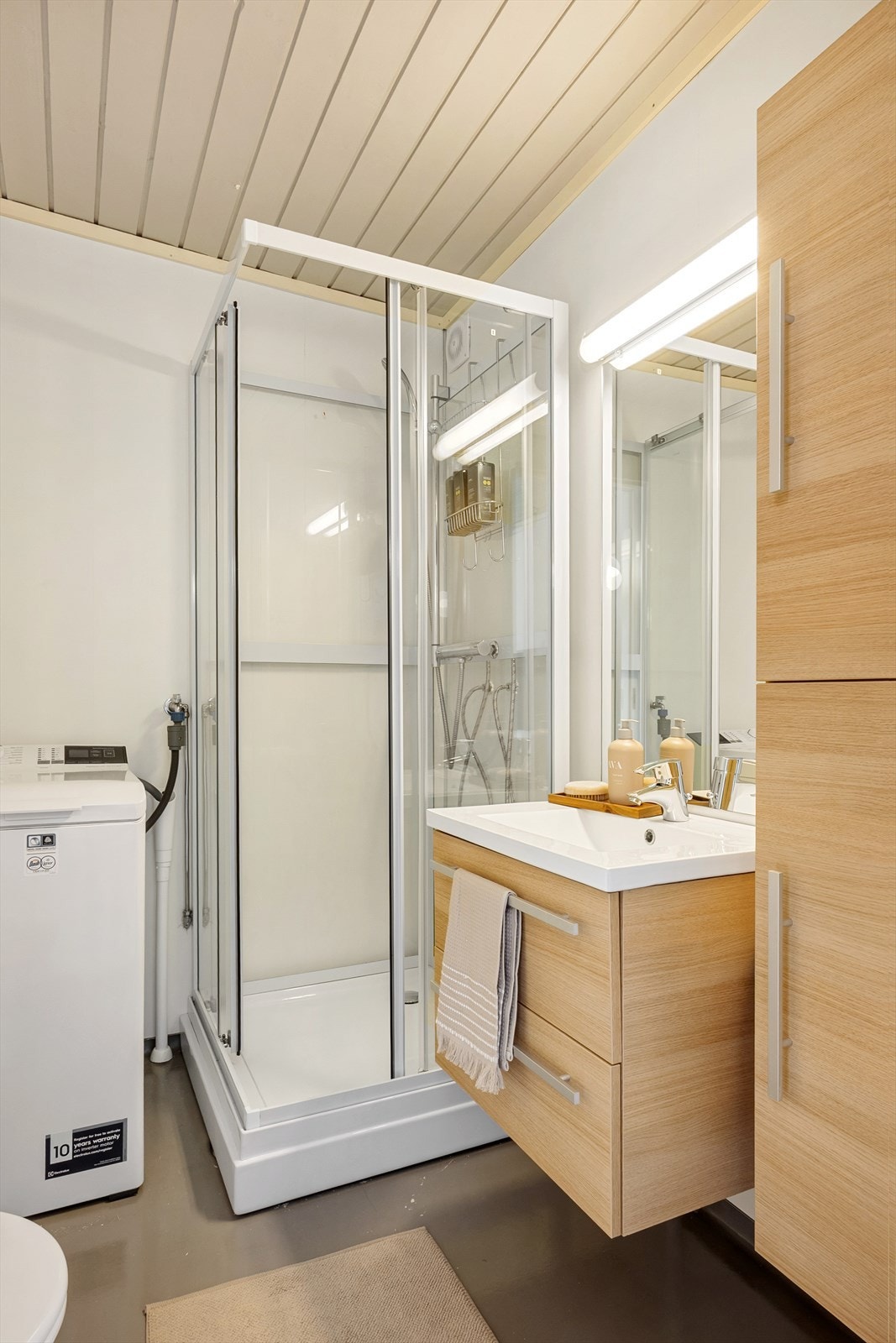 Badet er av eldre dato, med tidløse overflater og nyere baderomsplater. Innredningen består av servant med tilhørende skuffeseksjon, speil, toalett og dusjkabinett. Galleribilde