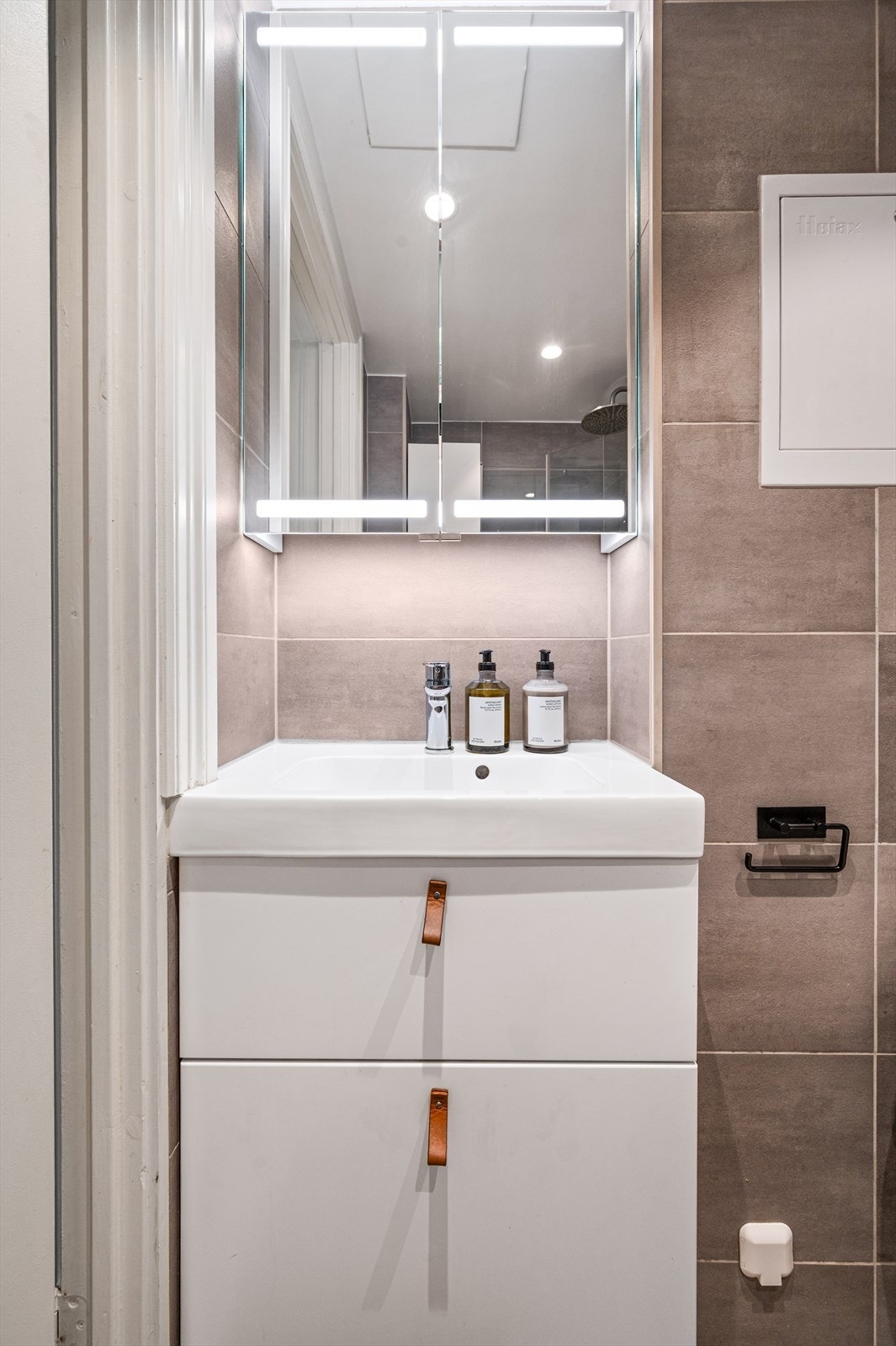 Innredet med vegghengt klosett, servant med innredning og speil med lys. Galleribilde