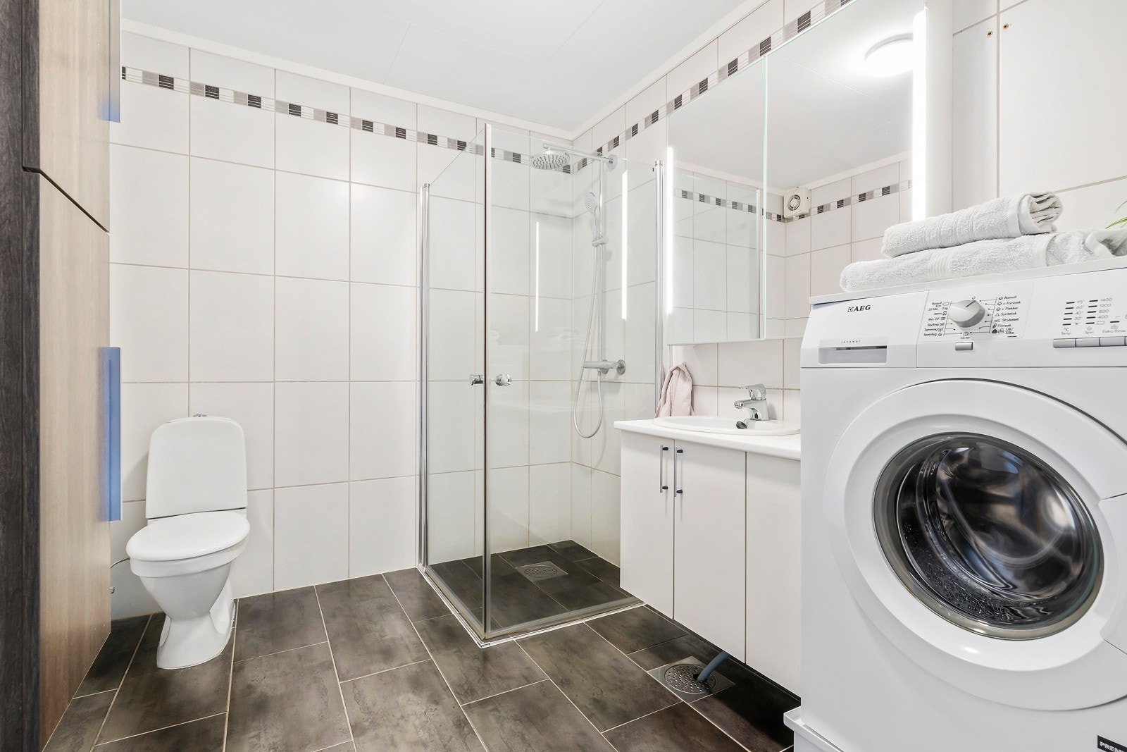 Helfliset bad med dusjnisje med innfellbare dører, og opplegg for vaskemaskin og tørketrommel. Galleribilde