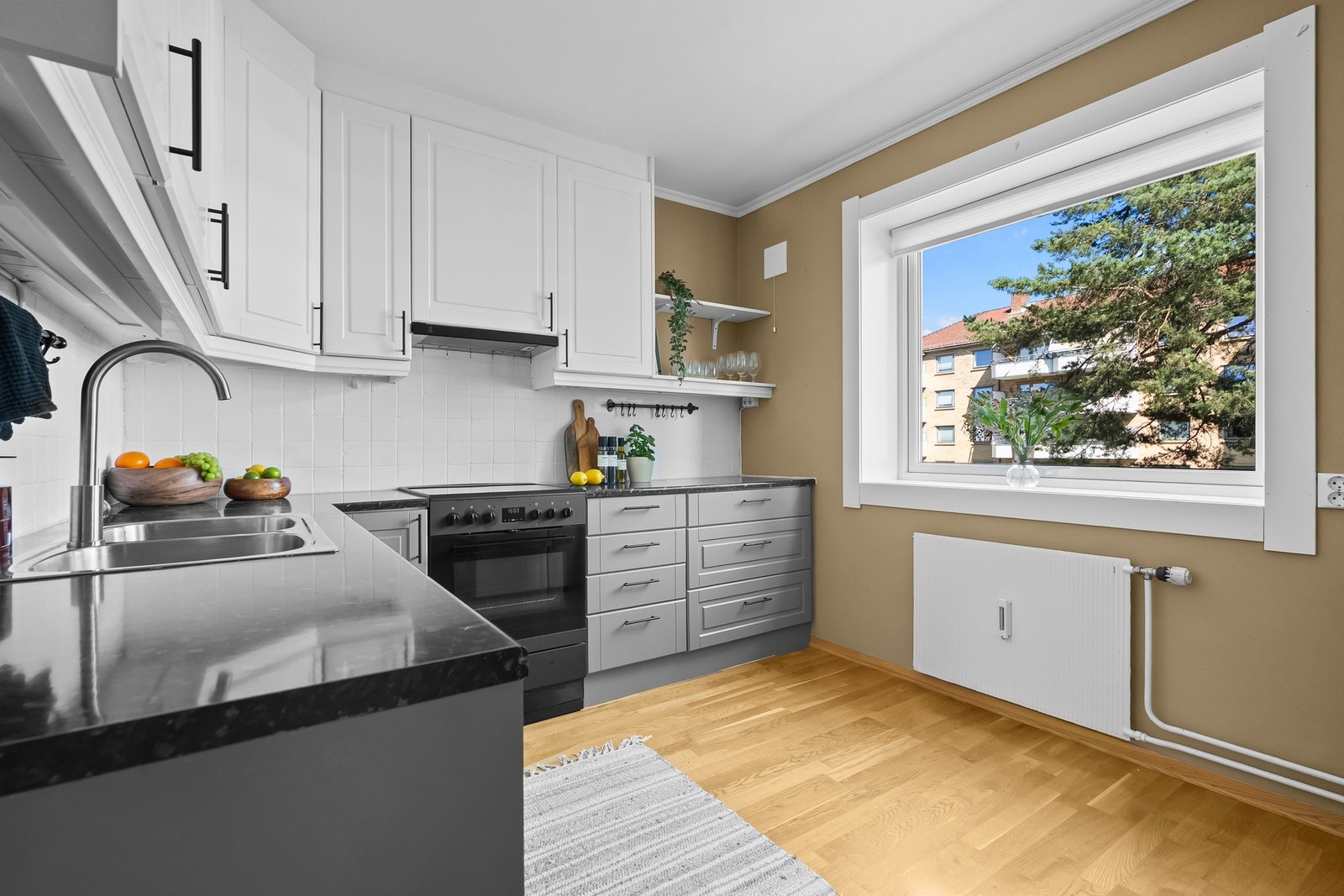 Leiligheten har et fint kjøkken med parkettgulv, beige vegger og stort vindu. Galleribilde