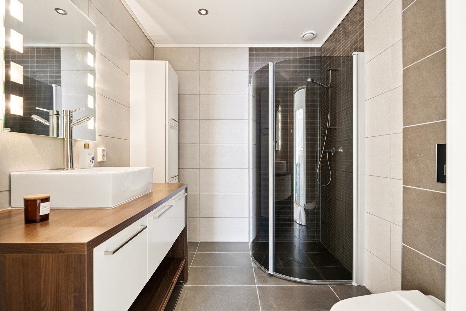 Badet har flislagt gulv med varmekabler. Innredet med baderomsinnredning med servant, vegghengt toalett og dusjhjørne Galleribilde