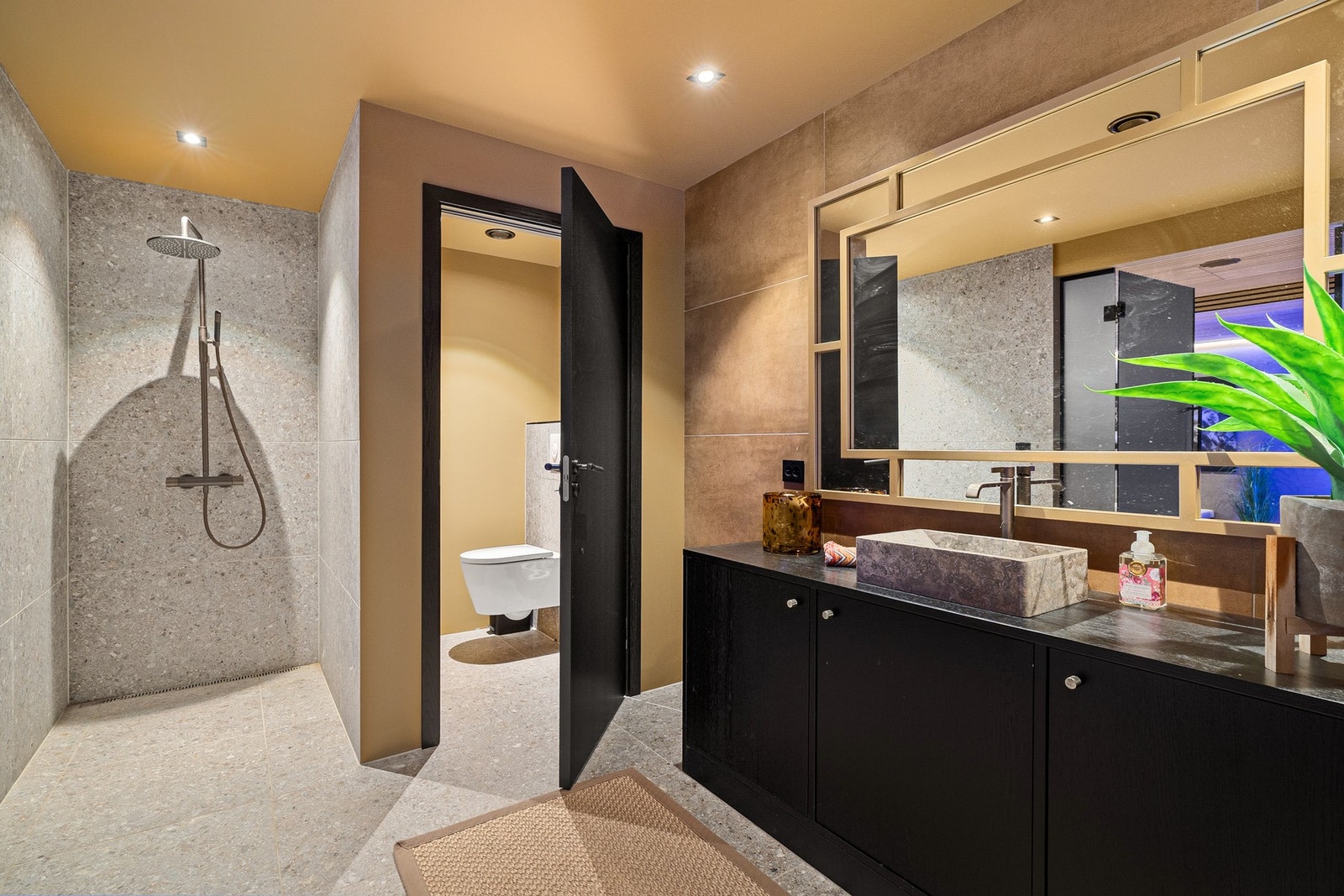 Baderom i tilknytning til spa-avdeling, med stilrene overflater, regnfallsdusj og separat toalettrom. Galleribilde