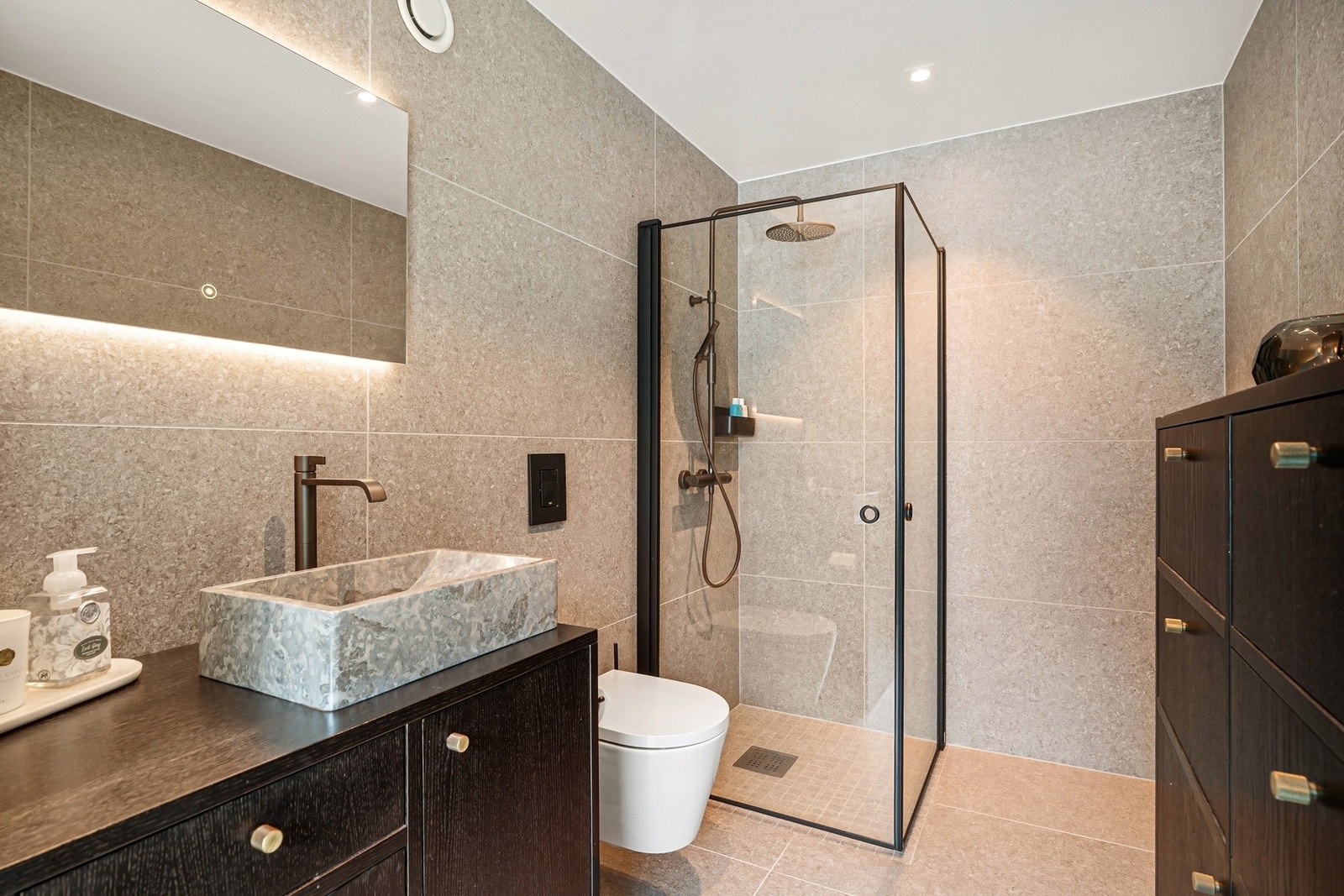 Badet har godt med oppbevaring, regnfalls dusj, vegg hengt WC og speil med lys. Galleribilde