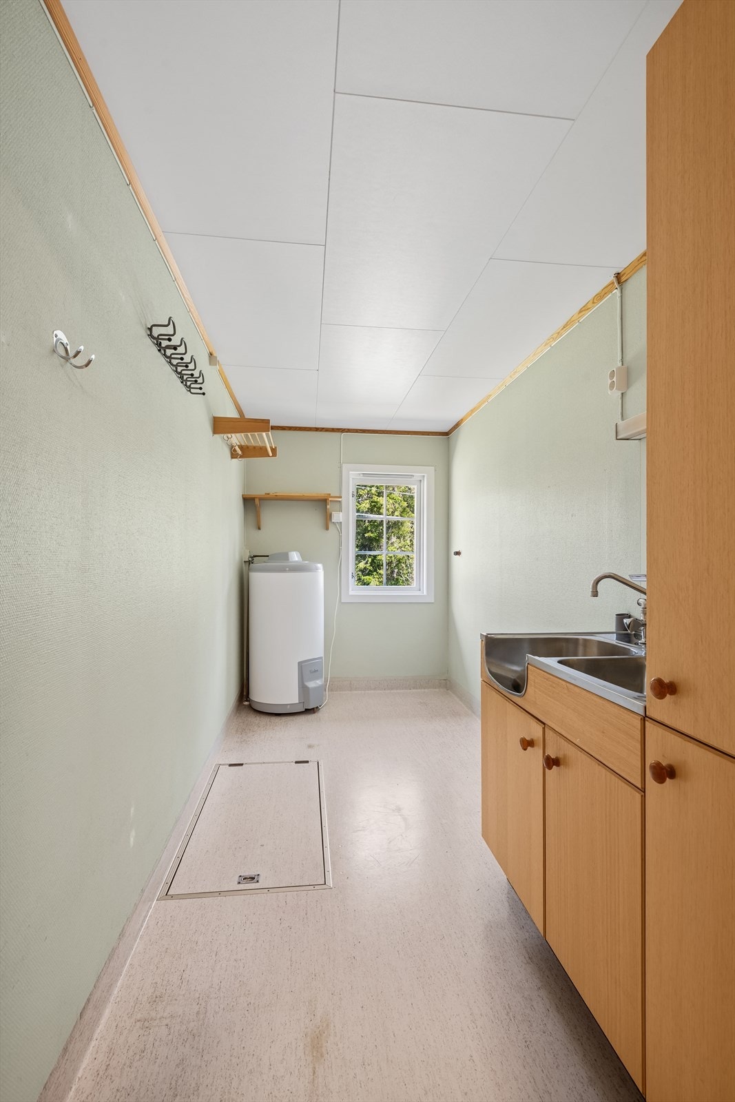 Vaskerom med belegg på gulvet og tapet på veggene, innredet med stålkum, høyskap og opplegg for vaskemaskin. Galleribilde