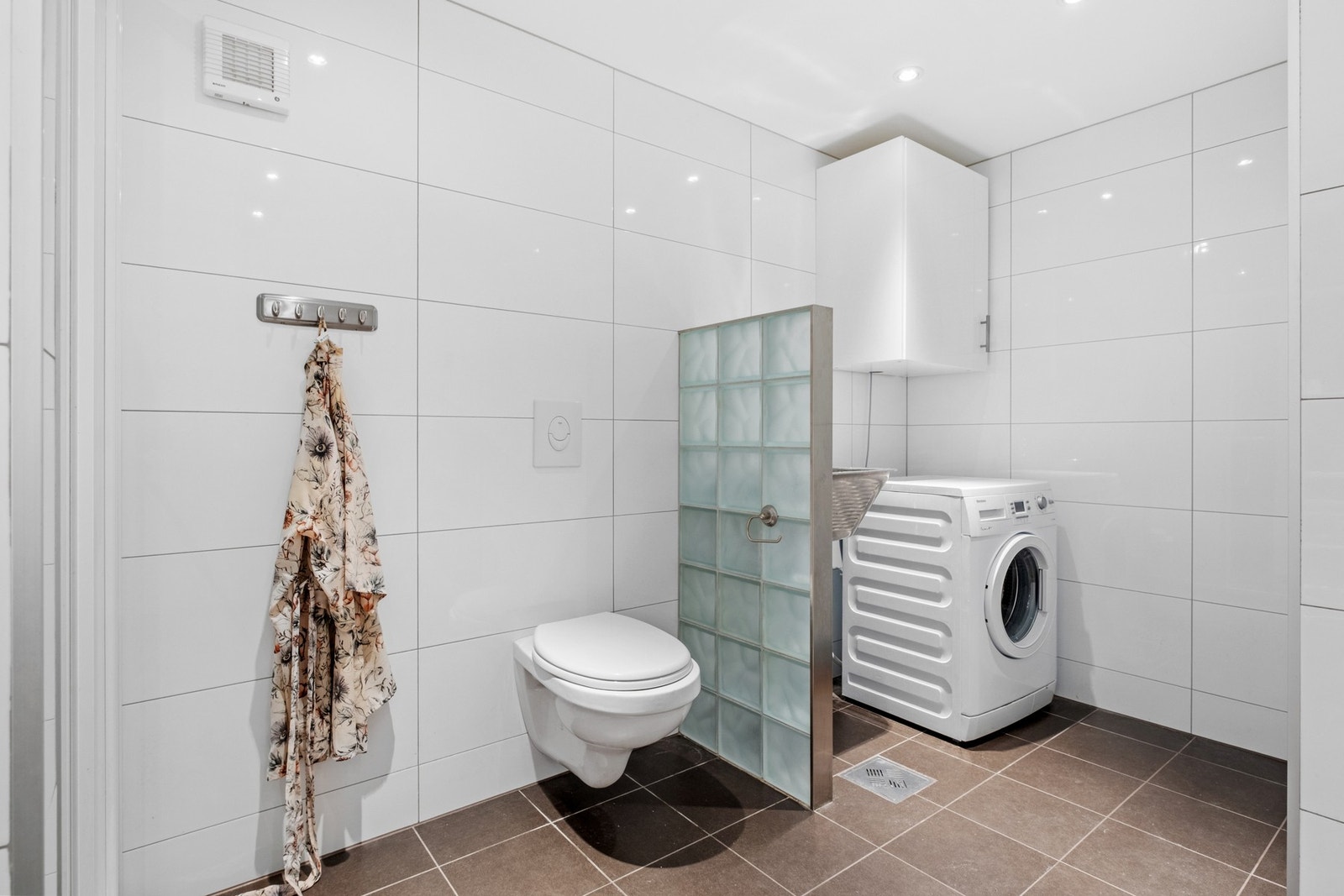 Badet er utstyrt med dusjnisje med glassdør, veggmontert wc, opplegg for vaskemaskin og utslagsvask. Galleribilde