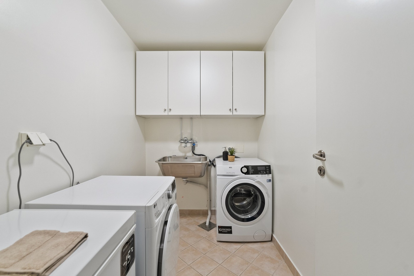 Eget vaskerom med flislagt gulv, utslagsvask, veggskap og plass til både vaskemaskin og tørketrommel. Galleribilde