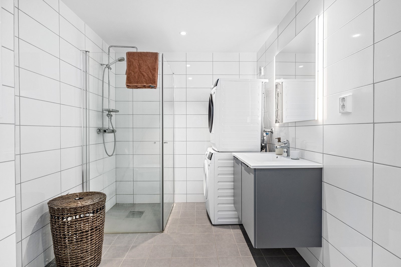 Pent flislagt baderom med dusjsone, toalett, servant med underskap, stort speil, og god plass til tørk- og vaskemaskin. Galleribilde