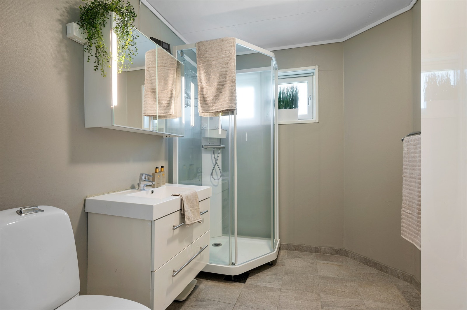 Pent bad på 4,5 kvm med flislagt gulv med varme, servantskap med overskap og speil med lys, dusjkabinett og toalett. Galleribilde