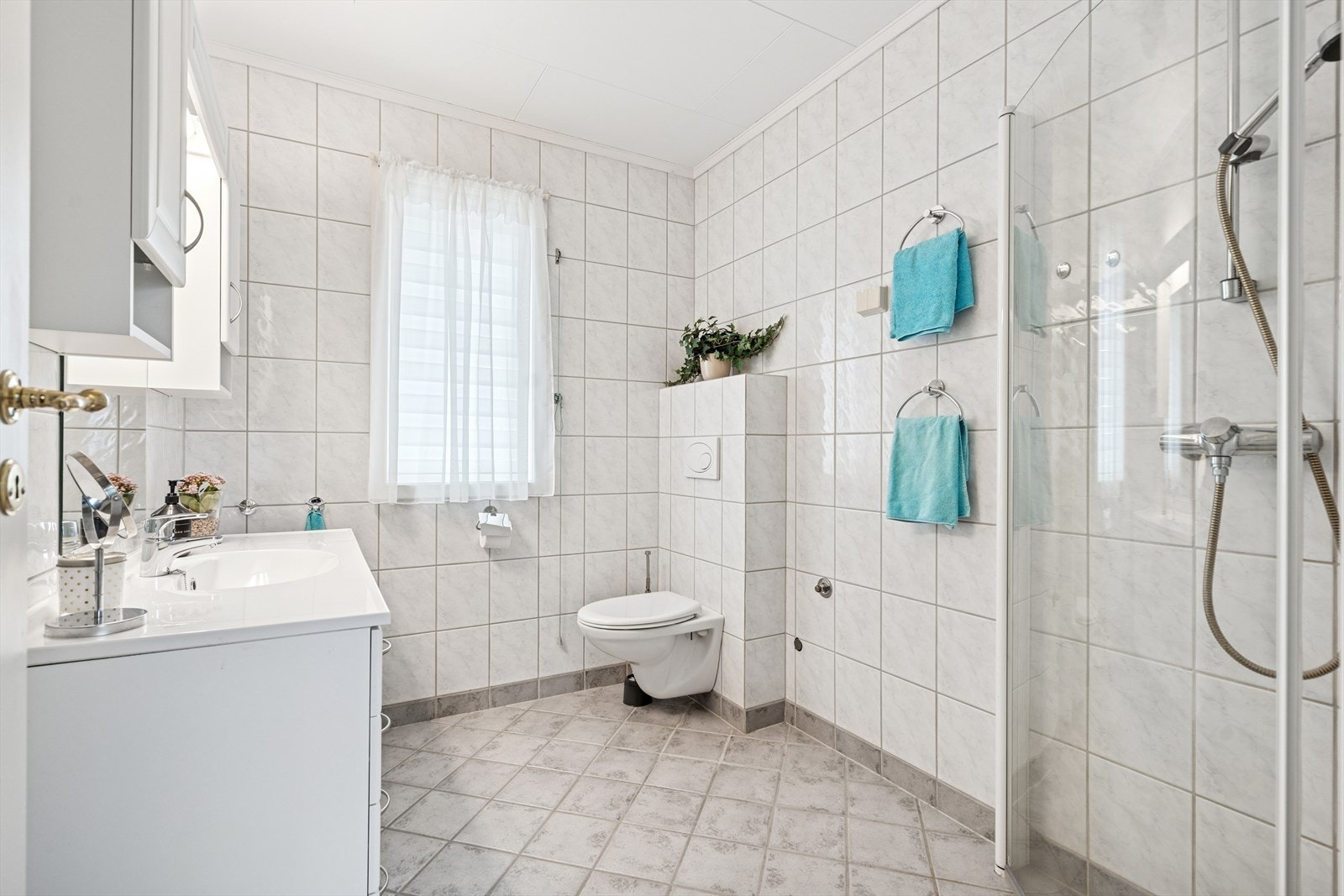 Rommet er innredet med vegghengt toalett, servant med underskap og dusjhjørne med glassvegger. Galleribilde