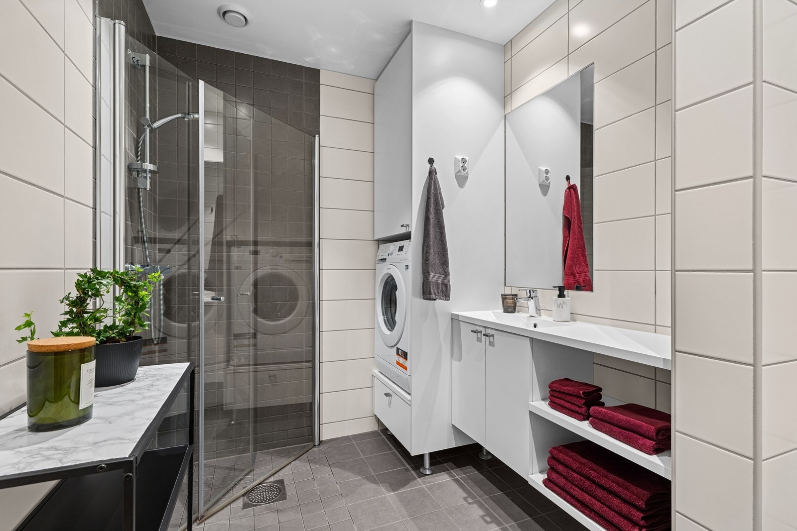 Badet er helfliset og delikat, og er utstyrt med servant med underskap, speil, dusjvegger, veggmontert wc, og opplegg for vaskemaskin. Galleribilde