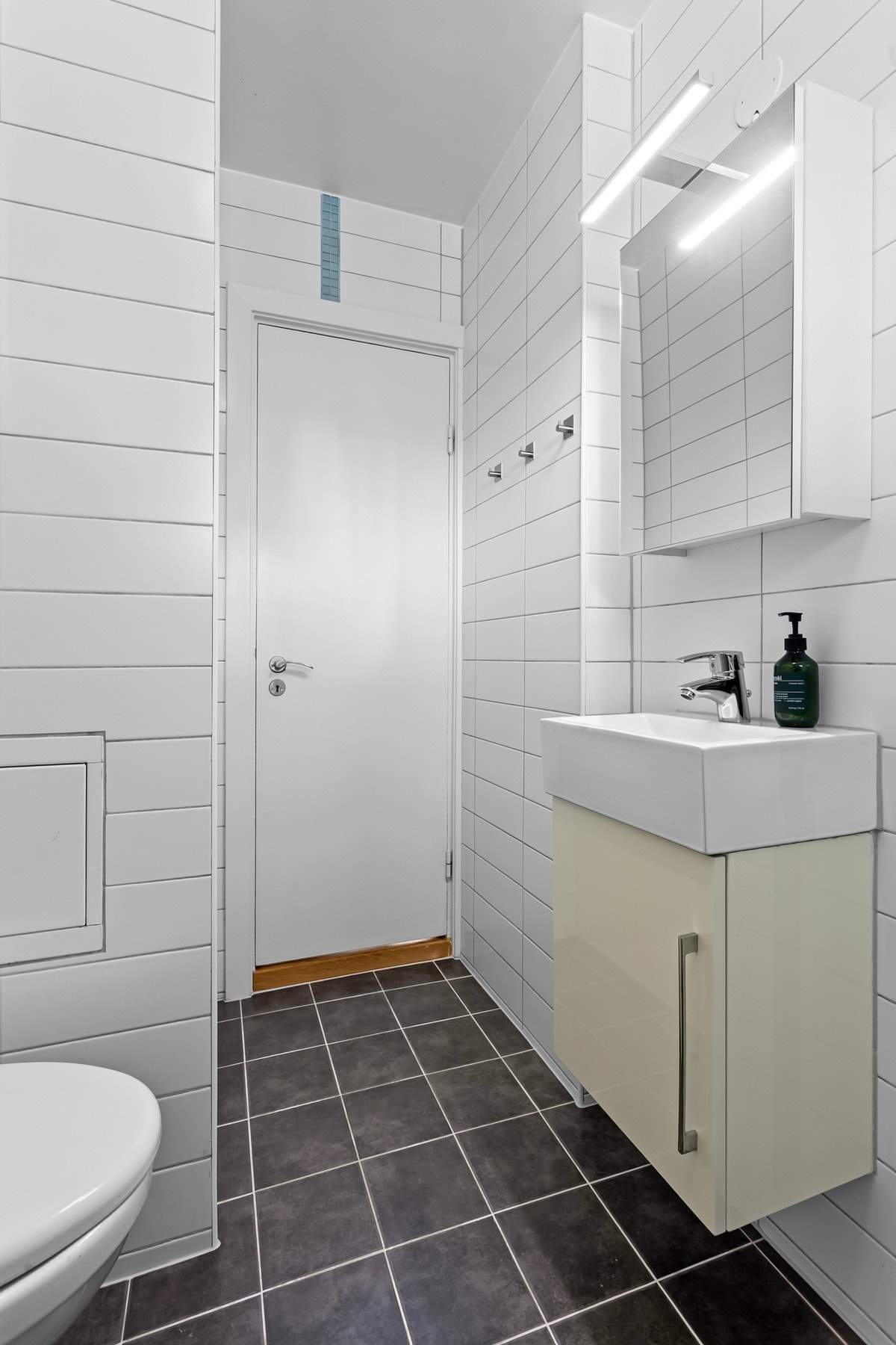 Håndvasken er plassert på et skap i høyglans, og over er det speilskap med belysning. Galleribilde