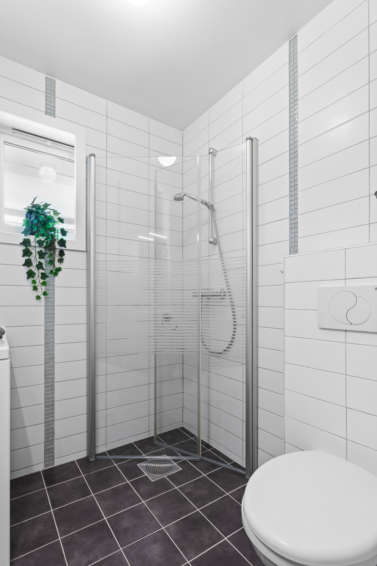 Badet er innredet med et vegghengt toalett, dusjhjørne med innfellbare glassdører og opplegg for vaskemaskin. Galleribilde