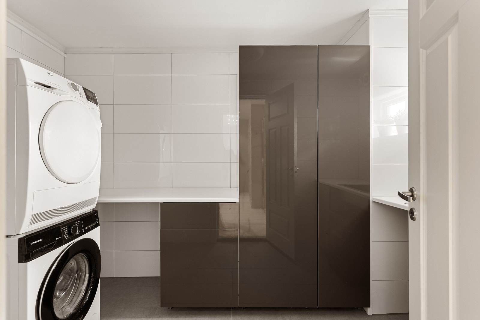 Innredningen består av høyskap med mørke høyglansfronter, hvit benkeplate med nedfelt vaskekum i stål og opplegg for vaskesøyle. Galleribilde