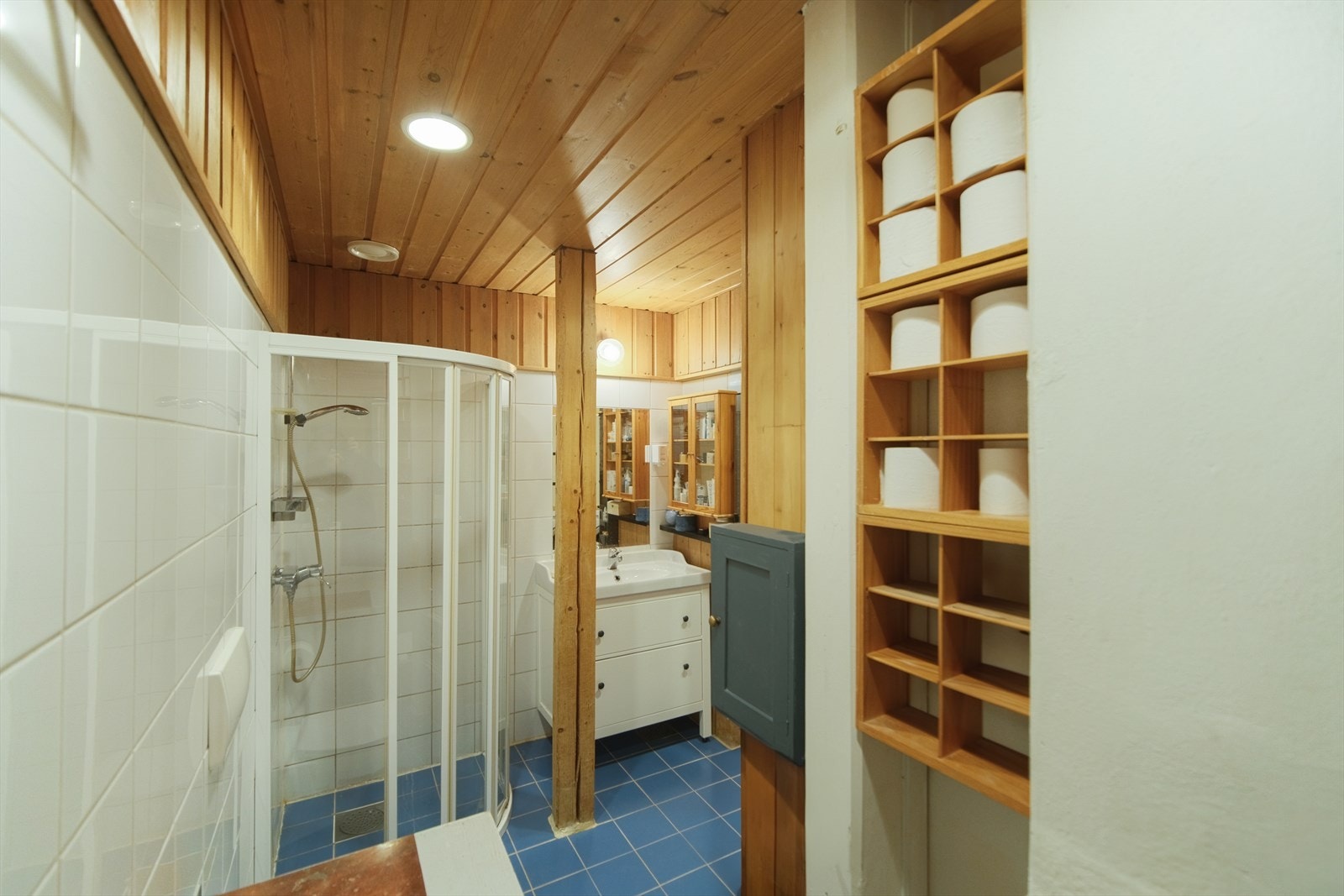 Eldre baderom med dusj på gulv med skyvedører, veggfestet klosett, servant med innredning og opplegg for vaskemaskin Galleribilde