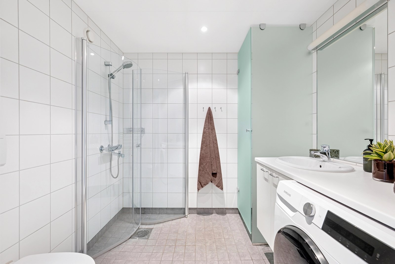 Pent flislagt bad bestående av vegghengt wc, servant med underskap, innfliset speil med overlys og inn-/utadslående dusjdører Galleribilde