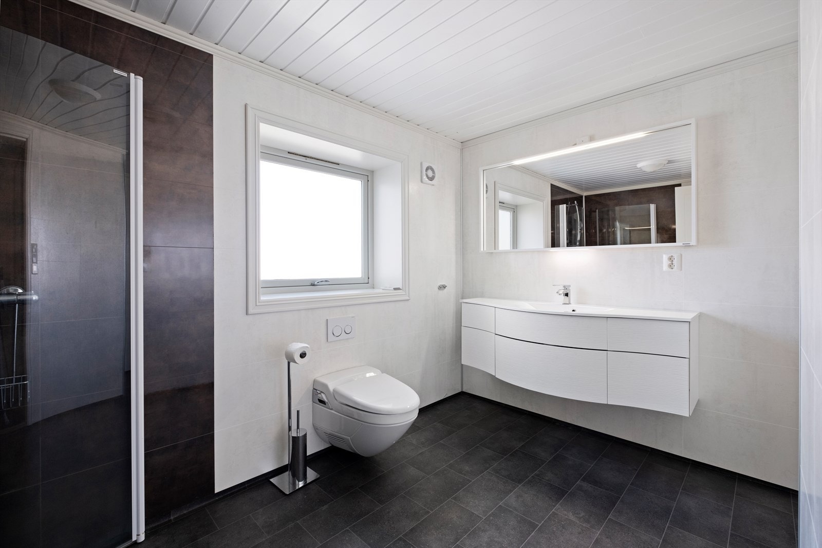 Badet har hvit innredning med helstøpt servant/plate over underskap og stort speil Galleribilde