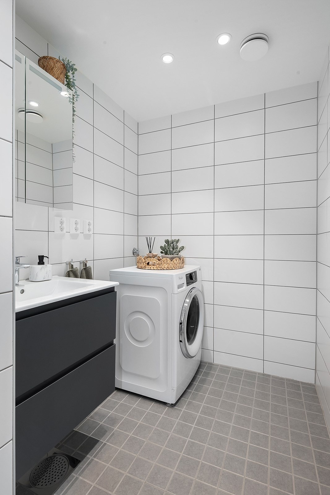 Badet inneholder servantskap med speil, dusjdører i glass, vegghengt toalett og opplegg for vaskemaskin. Galleribilde