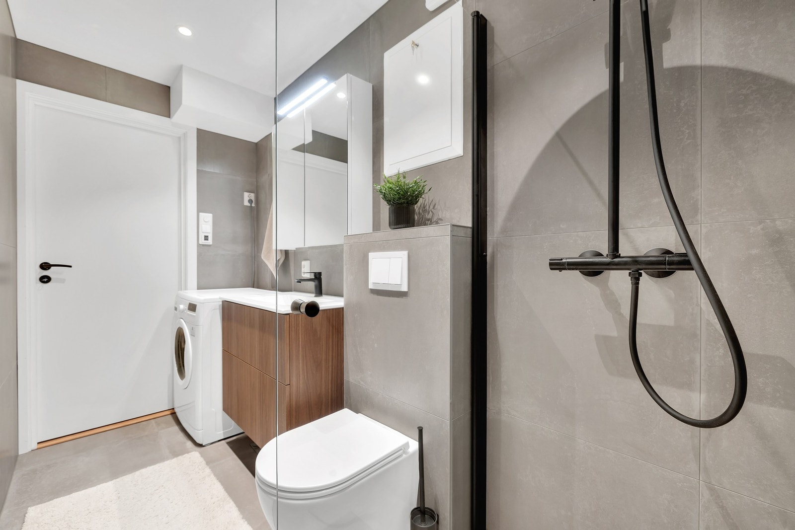 Svært flotte materialvalg med 60x60-flis, sorte detaljer i dusj og servant, vegghengt WC og opplegg for vaskemaskin. Galleribilde